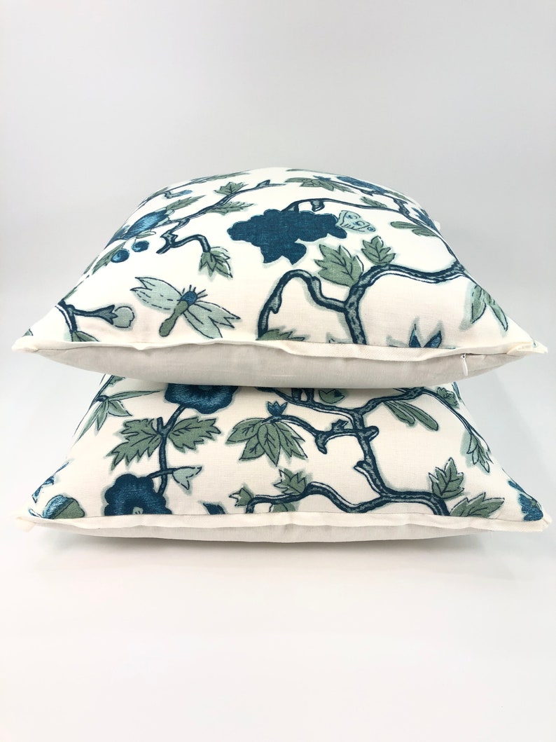 May include: Two white throw pillows with a blue and green floral pattern. The pillows are stacked on top of each other.