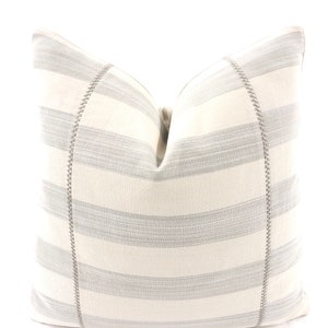 May include: A white and gray striped pillow with a gray stitched border. The pillow is made of a soft, textured fabric.