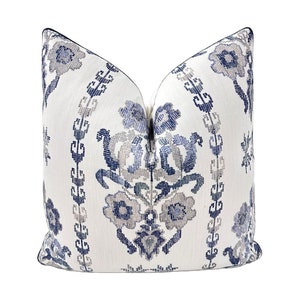 May include: A white throw pillow with a blue and gray floral pattern. The pillow has a navy blue trim.
