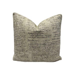 Puede incluir: Un cojín decorativo con fondo beige y diseño de escritura negra. El cojín tiene un aspecto texturizado y una estética clásica y vintage. La escritura cubre toda la superficie del cojín.