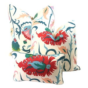 Puede incluir: Tres cojines decorativos con fondo crema y un vibrante estampado floral en rojo, turquesa, rosa y verde. Los cojines varían en tamaño y forma, con un ribete turquesa en el cojín más pequeño.