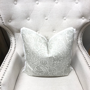 May include: A white tufted armchair with a light gray patterned pillow with a white border.