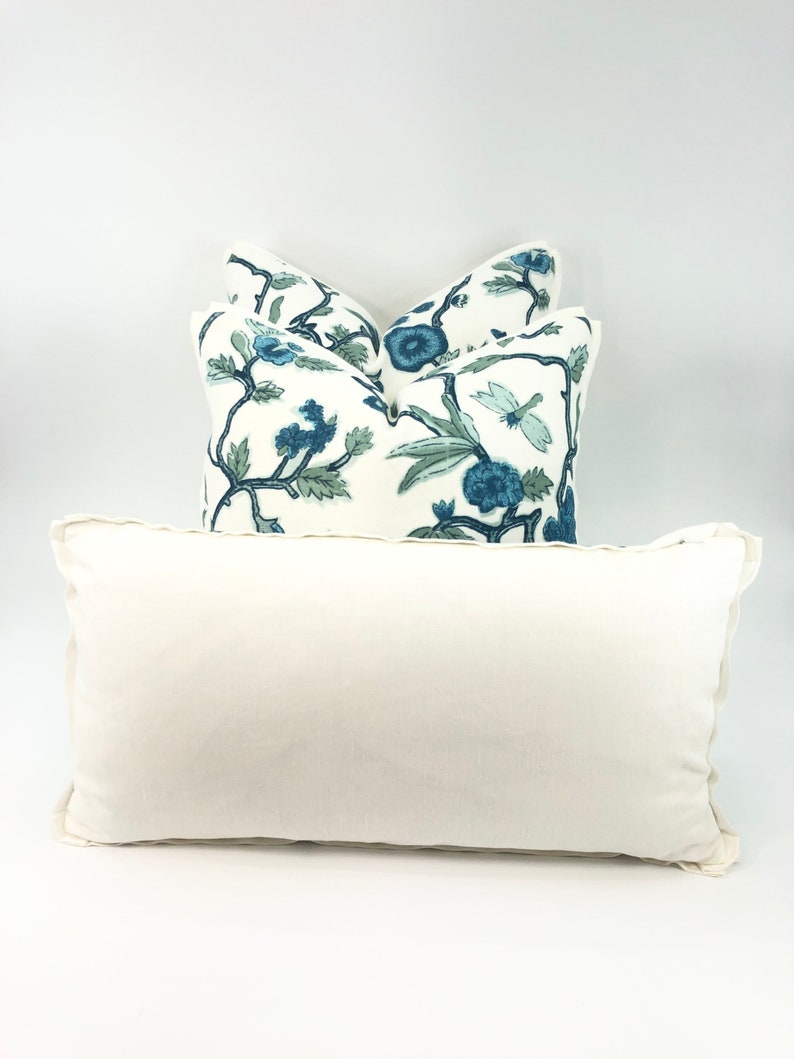 May include: Three decorative throw pillows with a white background and blue floral pattern. The pillows are stacked on top of each other. The top pillow is a solid white color.