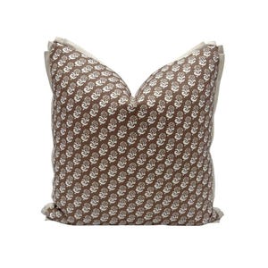 May include: A decorative throw pillow with a brown paisley pattern and a neutral-colored border. The pillow features a repeating white floral design on a brown background. The pillow is square and has a soft, inviting appearance.