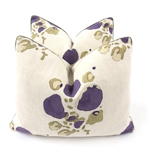 May include: Two square throw pillows with a white linen fabric and a purple and green abstract pattern.