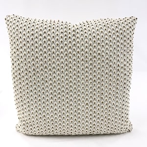 Puede incluir: Una almohada blanca con un patrón sutil de pequeños círculos marrones en relieve. La almohada es cuadrada y tiene una superficie suave y texturizada.