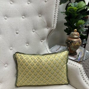 May include: A yellow and green patterned throw pillow with a green border sits on a white armchair with tufted upholstery.