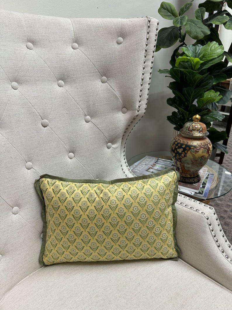 May include: A yellow and green patterned throw pillow with a green border sits on a white armchair with tufted upholstery.