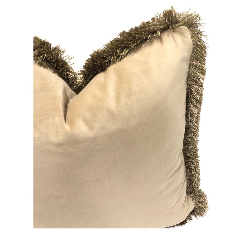 May include: A beige velvet pillow with a gold fringe trim around the edges.