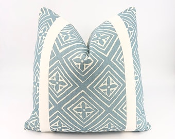 Puede incluir: Una almohada de color azul y blanco con un ribete blanco alrededor de los bordes. La almohada tiene un diseño geométrico con flores blancas.