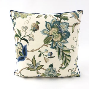 Puede incluir: Una almohada blanca con un patrón floral azul y verde. La almohada tiene un ribete azul marino.