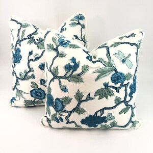 May include: Two white throw pillows with a blue and green floral pattern. The pillows have a simple, elegant design and would add a touch of sophistication to any room.