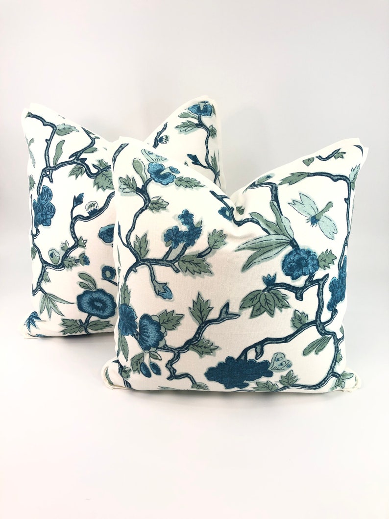 May include: Two white throw pillows with a blue and green floral pattern. The pillows have a simple, elegant design and would add a touch of sophistication to any room.