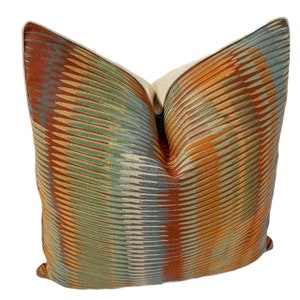 Puede incluir: Una almohada decorativa con un patr&oacute;n geom&eacute;trico en tonos naranja, marr&oacute;n, verde y azul. La almohada tiene un respaldo de lino beige.