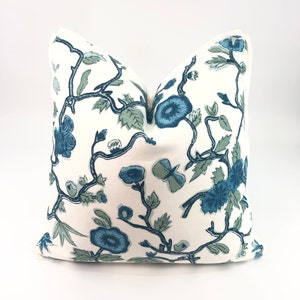 May include: A white pillow with a blue and green floral pattern. The pillow features a repeating design of stylized flowers and branches.