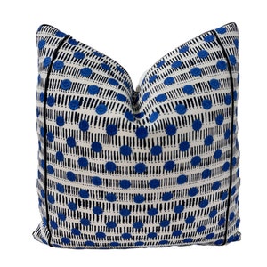 May include: A white and blue patterned throw pillow with a black trim. The pillow features a repeating pattern of blue circles and black lines.