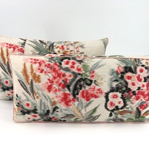 May include: Two decorative throw pillows with a floral pattern. The pillows are made of a light-colored fabric with a subtle texture. The floral pattern features pink, red, black, and green colors.