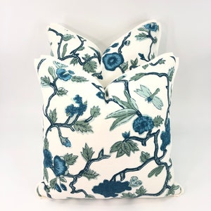 May include: Two white throw pillows with a blue and green floral pattern. The pillows are stacked on top of each other.