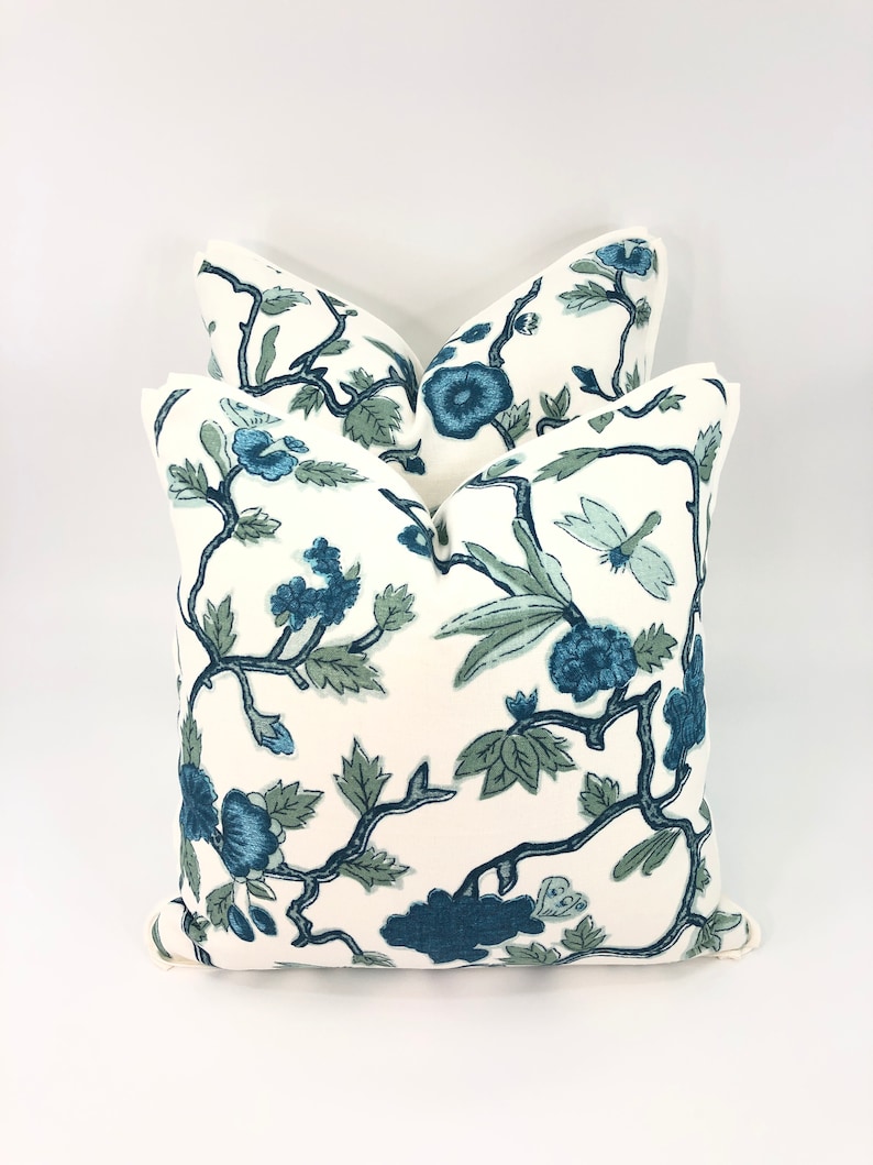 May include: Two white throw pillows with a blue and green floral pattern. The pillows are stacked on top of each other.