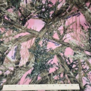 May include: Pink camouflage fabric with a pattern of brown branches and green foliage. A ruler is at the bottom of the image, showing measurements in inches.