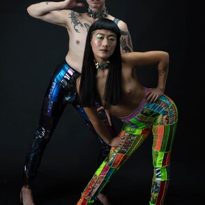 K&ouml;nnte beinhalten: Zwei Personen tragen bunte Patchworkhosen. Eine Person tr&auml;gt schwarze Hosen mit einem blauen, schimmernden Glanz. Die andere Person tr&auml;gt leuchtend gr&uuml;ne, gelbe, orange und rosa Patchworkhosen. Beide Personen tragen schwarze Choker-Halsketten.