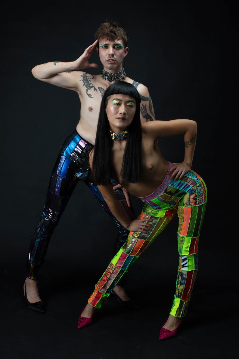 K&ouml;nnte beinhalten: Zwei Personen tragen bunte Patchworkhosen. Eine Person tr&auml;gt schwarze Hosen mit einem blauen, schimmernden Glanz. Die andere Person tr&auml;gt leuchtend gr&uuml;ne, gelbe, orange und rosa Patchworkhosen. Beide Personen tragen schwarze Choker-Halsketten.