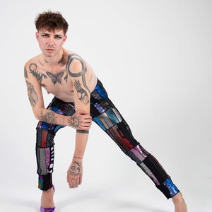 K&ouml;nnte beinhalten: Eine Person tr&auml;gt eine Hose aus Patchwork mit verschiedenen Farben und Texturen, darunter Schwarz, Blau, Rot und Silber. Sie tr&auml;gt lilafarbene High Heels und hat mehrere Tattoos auf ihren Armen und ihrer Brust.