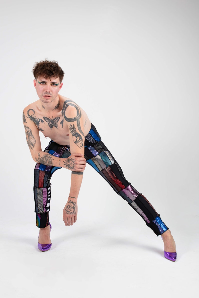 K&ouml;nnte beinhalten: Eine Person tr&auml;gt eine Hose aus Patchwork mit verschiedenen Farben und Texturen, darunter Schwarz, Blau, Rot und Silber. Sie tr&auml;gt lilafarbene High Heels und hat mehrere Tattoos auf ihren Armen und ihrer Brust.