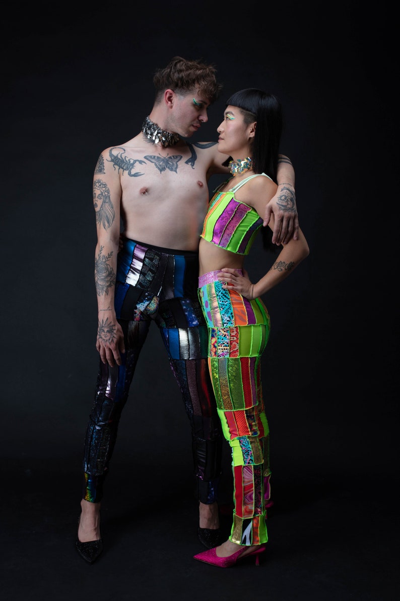 K&ouml;nnte beinhalten: Zwei Personen tragen bunte Patchworkhosen und Oberteile. Die Person links tr&auml;gt eine silberne Halskette und hat T&auml;towierungen auf den Armen. Die Person rechts tr&auml;gt ein gr&uuml;n-pinkes Oberteil und eine silberne Halskette. Sie schauen sich an.