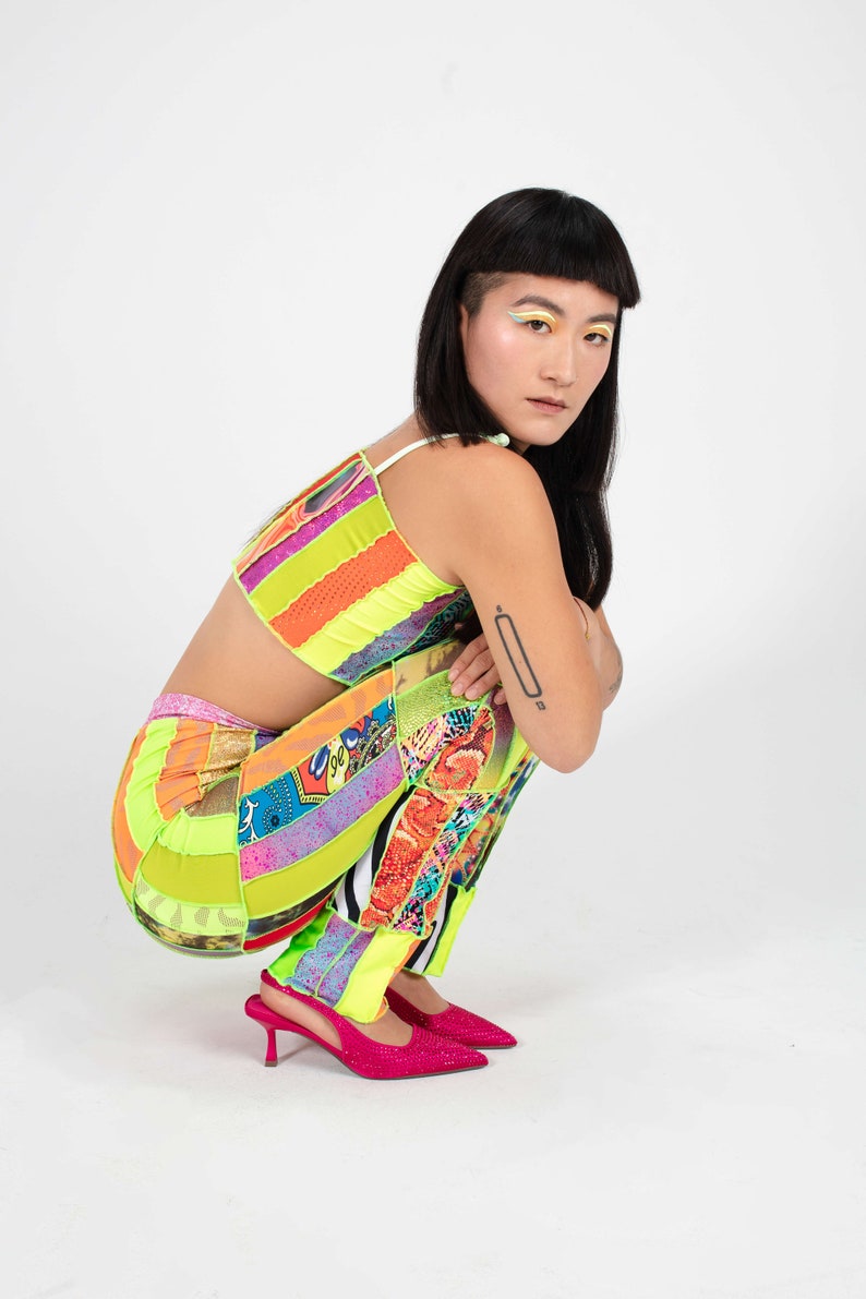 K&ouml;nnte beinhalten: Eine Frau tr&auml;gt ein hellgr&uuml;nes, orangefarbenes und rosafarbenes Patchwork-Crop-Top und eine passende Hose. Sie tr&auml;gt rosa High Heels und hat farbenfrohes Augen-Make-up.