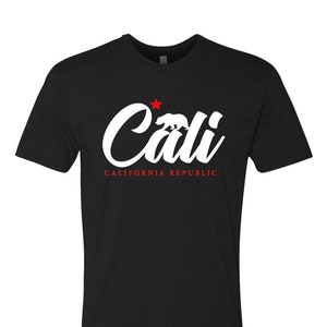 May include: Black t-shirt with a white graphic of the word "Cali" in a stylized font. A red star and a white silhouette of a bear are above the word. The text "CALIFORNIA REPUBLIC" is below the word "Cali".