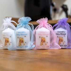May include: Four white candles in organza bags, each with a Winnie the Pooh graphic and the text "Hannah's Baby Shower" and a date. The bags are in white, blue, pink, and purple.