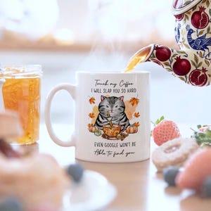 May include: A white ceramic mug with a black handle and the text "But First, Coffee" in a black, handwritten-style font. The mug sits on a white surface.