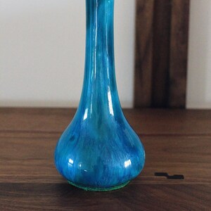 May include: A blue ceramic vase with a narrow neck and a rounded base. The vase has a marbled, swirled pattern in shades of blue and green.