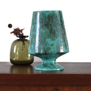 Peut inclure: Un vase en céramique bleu turquoise avec une base large et un sommet évasé. Le vase a un glaçage marbré et moucheté.