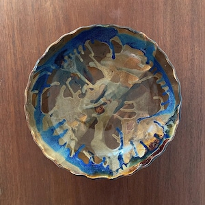 May include: A ceramic bowl with a scalloped edge and a blue and brown glaze. The glaze has a drip effect, creating a unique and abstract design.