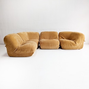 May include: A modular, mid-century modern sofa set in a warm, golden-brown color. The set includes a corner sectional, a single seat, and a rounded armchair. The plush, upholstered pieces are arranged against a white backdrop.
