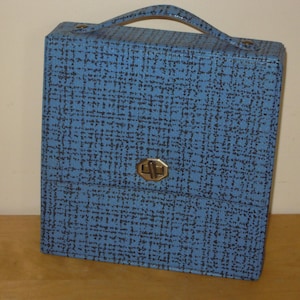 Peut inclure: Une mallette de transport vintage bleue et noire à motifs, avec une poignée et un fermoir en métal. Le boîtier rectangulaire est fait d'un matériau texturé. La poignée incurvée est fixée au sommet. Idéal pour le rangement.