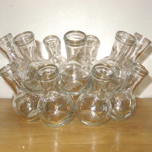 May include: A clear glass vase with multiple openings, each with a rounded base and a narrow neck. The vase is designed to hold multiple stems or small bouquets. The glass is transparent, allowing the contents to be visible.