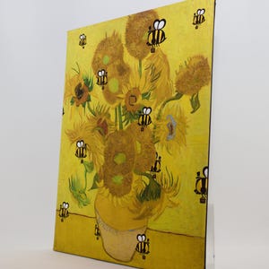 May include: A canvas print of Van Gogh's "Sunflowers" with cartoon bees superimposed on the flowers and background. The artwork features a yellow vase filled with sunflowers against a yellow backdrop, with black and yellow bees scattered across the image.