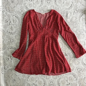 May include: A red dress with a V-neck and long sleeves. The dress is patterned with small white polka dots. The sleeves have a flared design. The dress is made of a lightweight fabric.