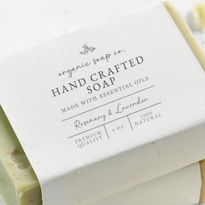 May include: Two rectangular bars of pale green hand crafted soap stacked together, wrapped in a white paper label with black text reading organic soap co. HAND CRAFTED SOAP MADE WITH ESSENTIAL OILS Rosemary & Lavender 4 OZ. PREMIUM QUALITY 100% NATURAL.