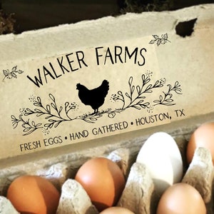 May include: A molded pulp egg carton containing twelve eggs of varying shades of brown and white. The lid features black printed text reading WALKER FARMS, FRESH EGGS, HAND GATHERED, HOUSTON, TX, and a graphic of a chicken surrounded by leafy branches.