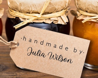 May include: Three glass jars filled with red, dark, and orange preserves. Each jar has a brown paper lid cover secured with raffia string. A rectangular brown paper tag hangs from the center jar with the text handmade by. Julia Wilson.