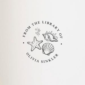 May include: A circular black ink stamp impression on the white page of an open book. The design features a starfish, a conch shell, and a scallop shell with the text FROM THE LIBRARY OF OLIVIA SINKLER arranged in a circle around the illustrations.