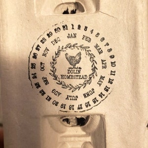 May include: A black and white calendar stamp with the text "DOLIN HOMESTEAD" and the months of the year in a circle around the text. The numbers 1 through 31 are also in a circle around the text.