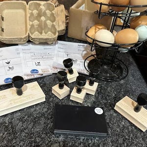 Peut inclure: Une collection de tampons en caoutchouc avec des manches en bois noir, un tampon encreur rectangulaire noir &eacute;tiquet&eacute; Black Felt, un porte-&oelig;ufs en fil m&eacute;tallique noir avec des &oelig;ufs color&eacute;s, des bo&icirc;tes &agrave; &oelig;ufs en carton et des formulaires de commande.