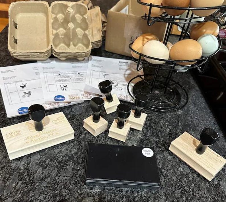 Peut inclure: Une collection de tampons en caoutchouc avec des manches en bois noir, un tampon encreur rectangulaire noir &eacute;tiquet&eacute; Black Felt, un porte-&oelig;ufs en fil m&eacute;tallique noir avec des &oelig;ufs color&eacute;s, des bo&icirc;tes &agrave; &oelig;ufs en carton et des formulaires de commande.