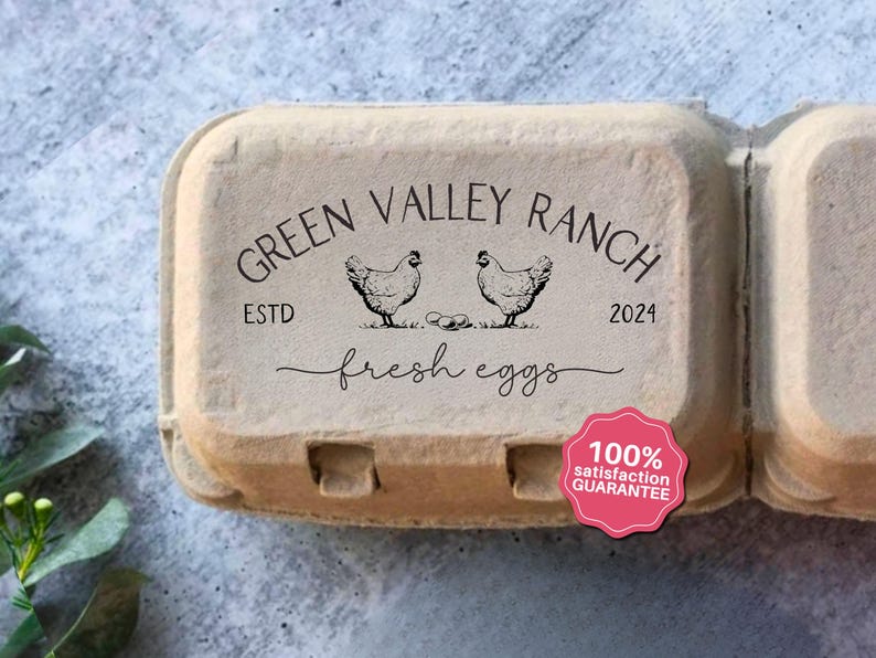 May include: A cardboard egg carton with the text "Green Valley Ranch" and "fresh eggs" in black script. Two chicken illustrations are above the text. A pink sticker reads "100% satisfaction guarantee".