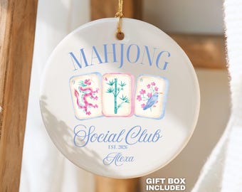 May include: A round white ceramic ornament featuring the blue text MAHJONG SOCIAL CLUB, EST. 2026, and the name Alexa. The center displays three mahjong tiles with illustrations of a pink dragon, green bamboo, and a blue bird with pink flowers.